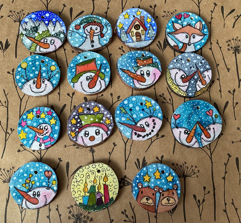 Colourful hand-painted round wooden winter ornaments with snowmen, a fox and a winter house.